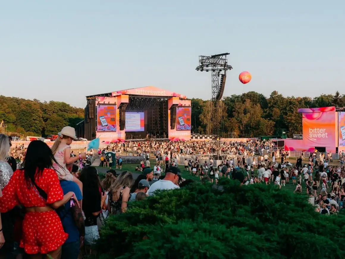 Tłum ludzi na festiwalu Bittersweet, scena w tle, różowe dekoracje i balon unoszący się na niebie.