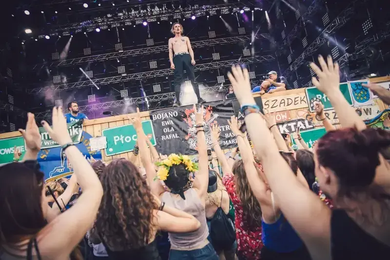 Energiczny tłum na czaplinek festiwal, z rękami w górze, podczas koncertu. Wokalista na scenie, fani szaleją.