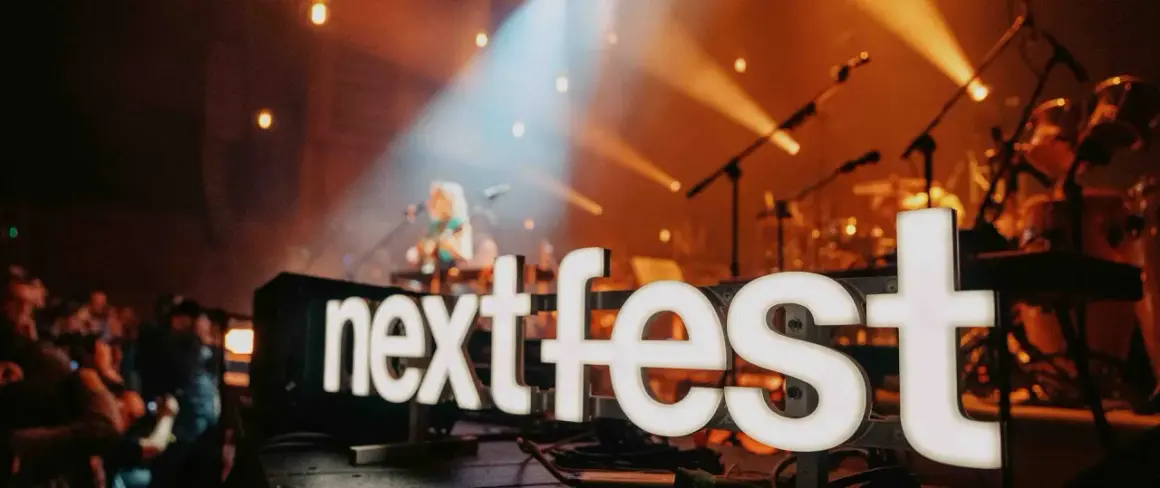 Światła sceny oświetlają napis "next fest" i artystkę grającą na gitarze.