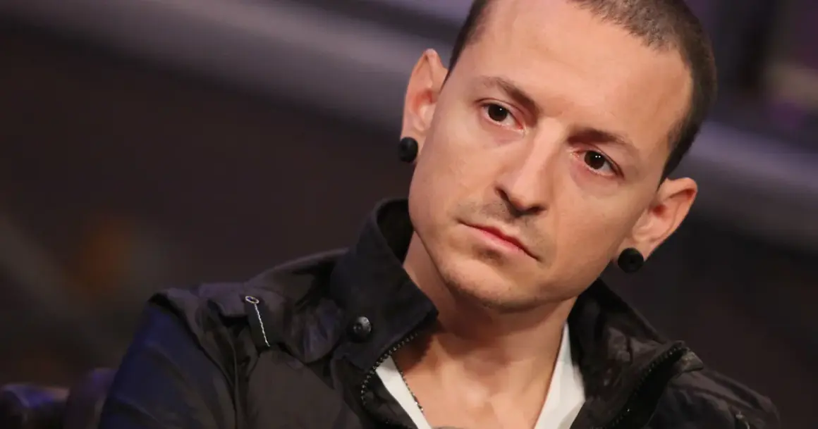 Chester Bennington z Linkin Park, z charakterystycznymi czarnymi tunelami w uszach, w czarnej kurtce.