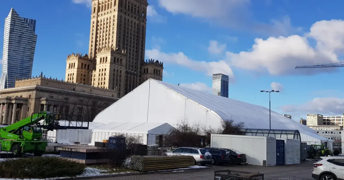 Biały namiot festiwalowy przed Pałacem Kultury w Warszawie, z nowoczesnymi wieżowcami w tle.