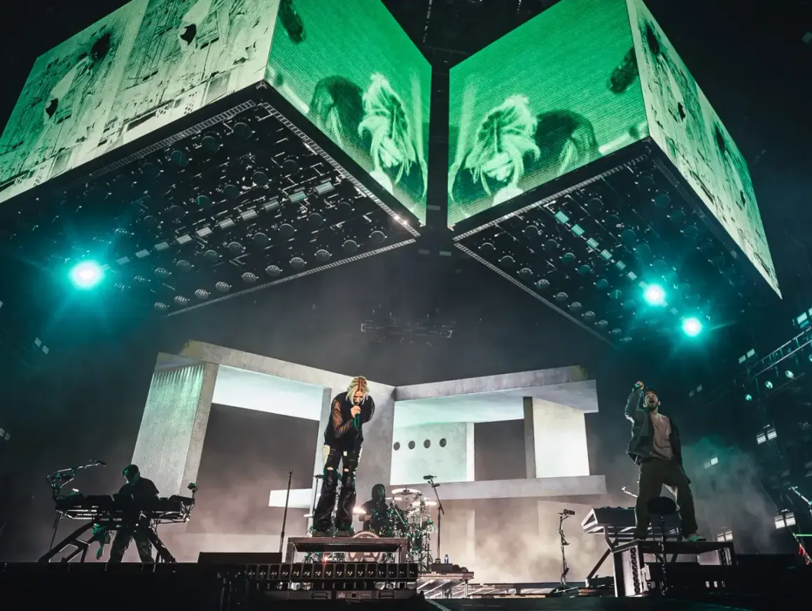 Energetyczny linkin park opener na scenie. Wokalista śpiewa, zespół gra, a nad nimi ogromne ekrany z zielonymi wizualizacjami.