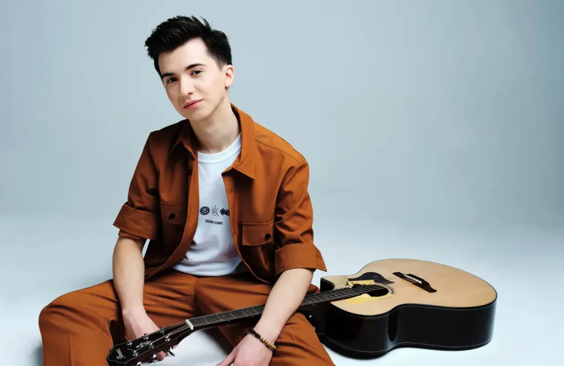 Marcin Patrzałek, młody muzyk, siedzi z gitarą, gotowy na koncert.