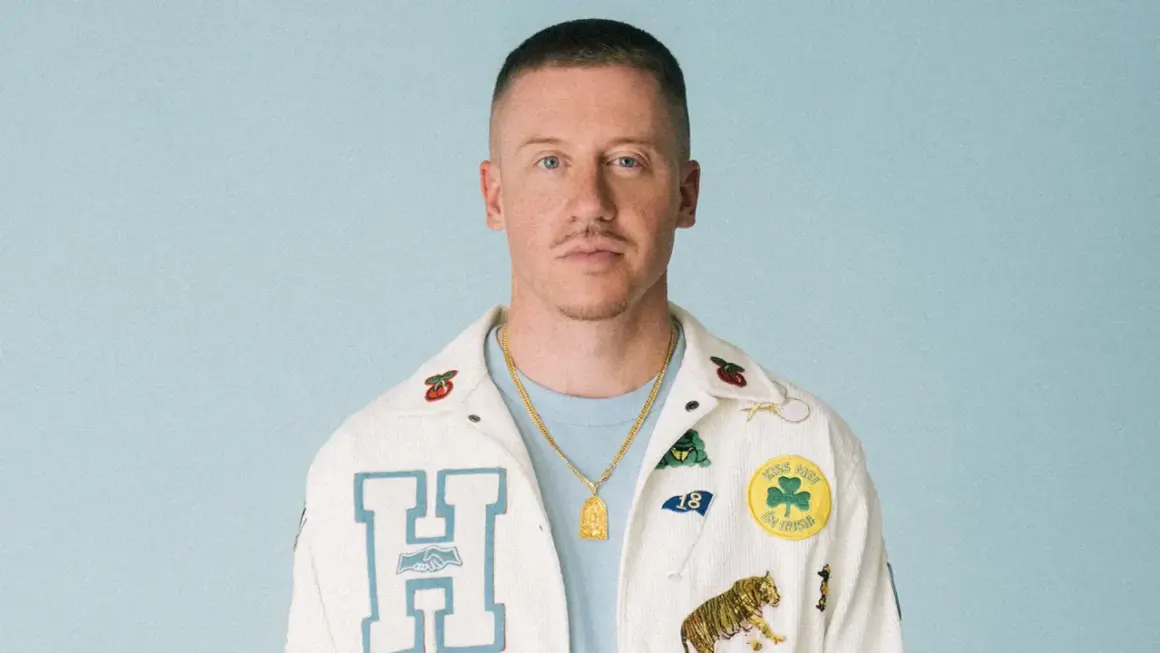 Macklemore w białej kurtce z naszywkami, gotowy na macklemore koncert polska.