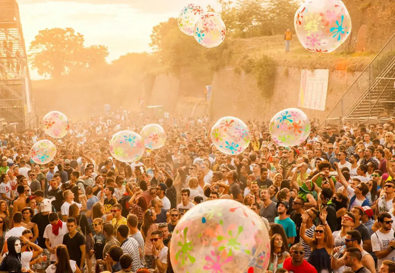 Tłum ludzi na festiwalu w letniej mgle, unoszą się wielkie, kolorowe balony.