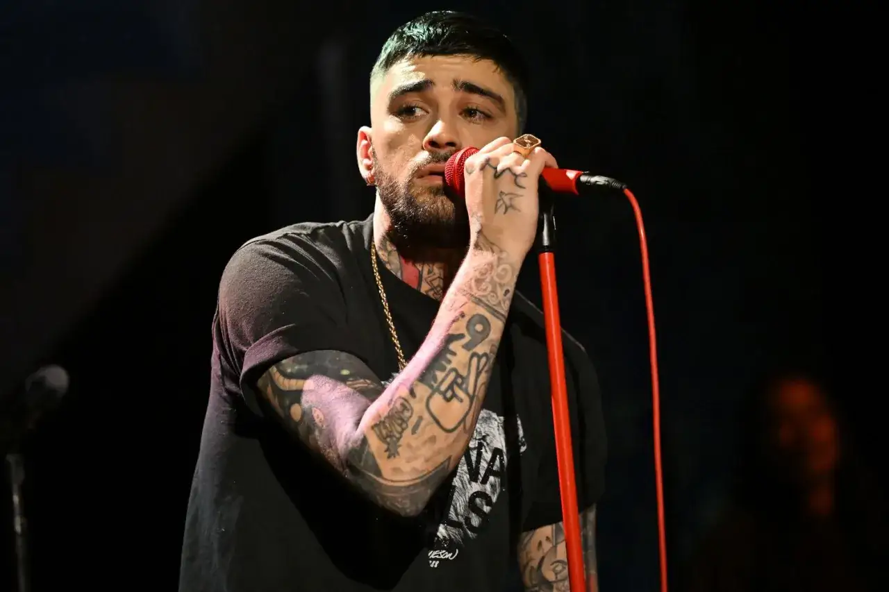 Zayn Malik, były członek One Direction, śpiewa do mikrofonu, jego ręce pokryte są tatuażami.