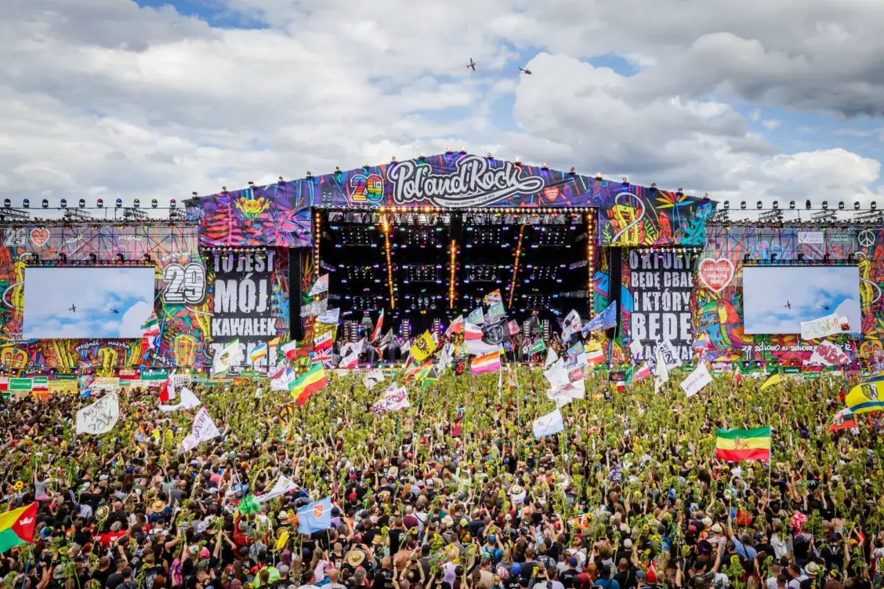 Tłum ludzi na festiwalu Poland Rock, z kolorową sceną i flagami. To jeden z największych festiwali w Polsce.