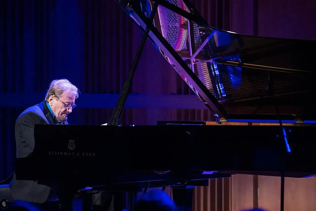 Polski pianista jazzowy w okularach pochyla się nad fortepianem Steinway & Sons, pogrążony w muzyce.