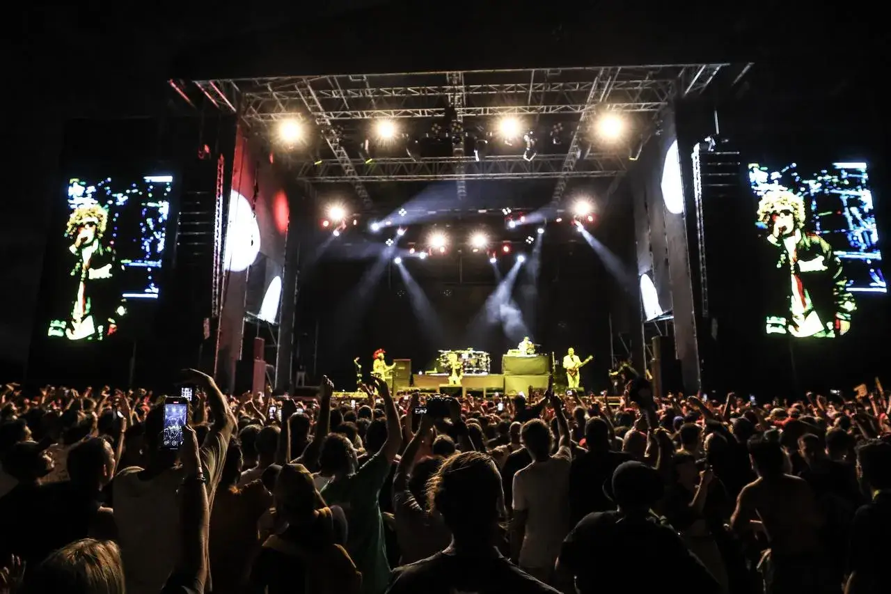 Tłum szaleje na koncercie Limp Bizkit. Na scenie gra zespół, a na telebimach widać wokalistę.