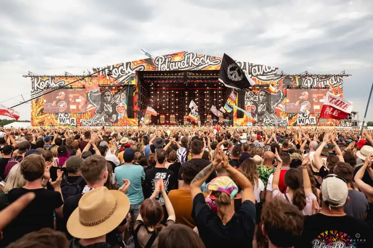 Tłum ludzi na koncercie Poland Rock 2026. Na scenie wielkie logo festiwalu, ekrany z grafikami i muzykami. Wszyscy bawią się świetnie.