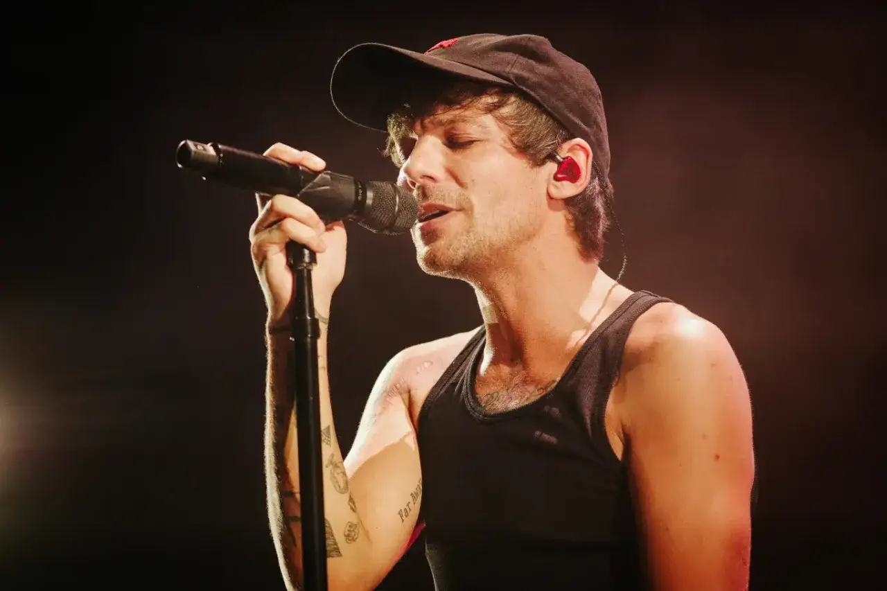 Louis Tomlinson Polska na koncercie, śpiewa do mikrofonu w czapce i czarnej koszulce.
