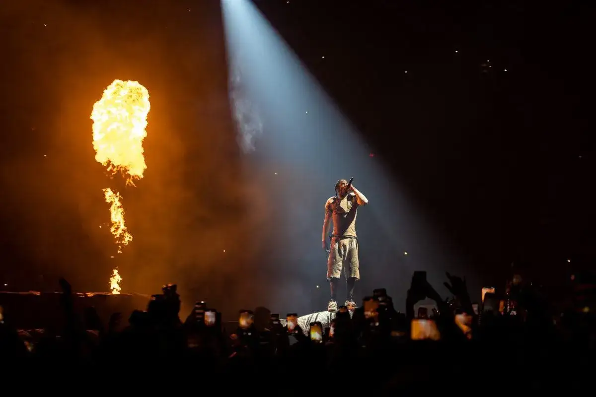 Travis Scott koncert: artysta na scenie, płomienie buchają w tle, tłum nagrywa telefonami.