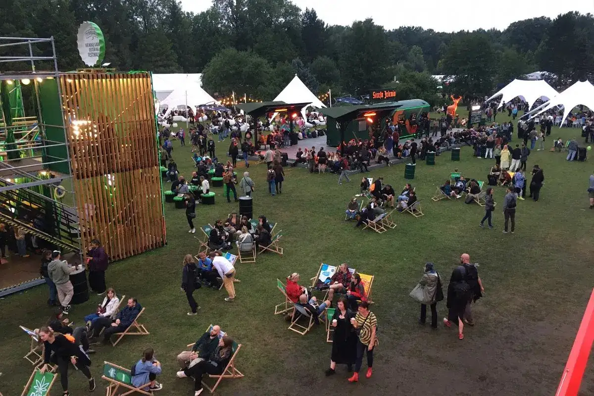 Ludzie odpoczywają na leżakach podczas festiwalu. W tle widać namioty i stoiska.