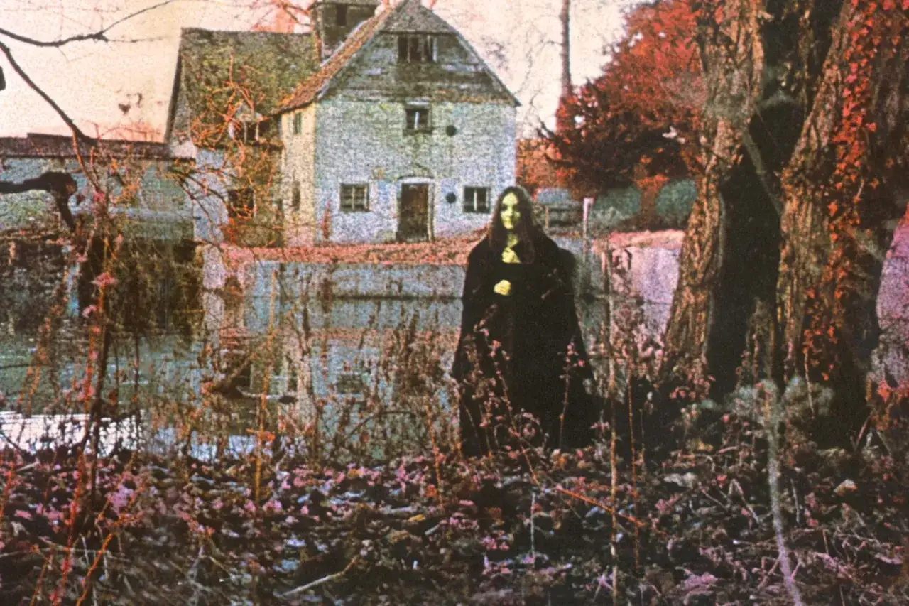 Mroczna postać w czerni przed domem, nawiązująca do okładki albumu zespołu Black Sabbath.
