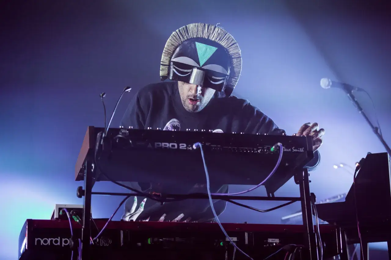 DJ z maską na twarzy tworzy muzykę na syntezatorze.