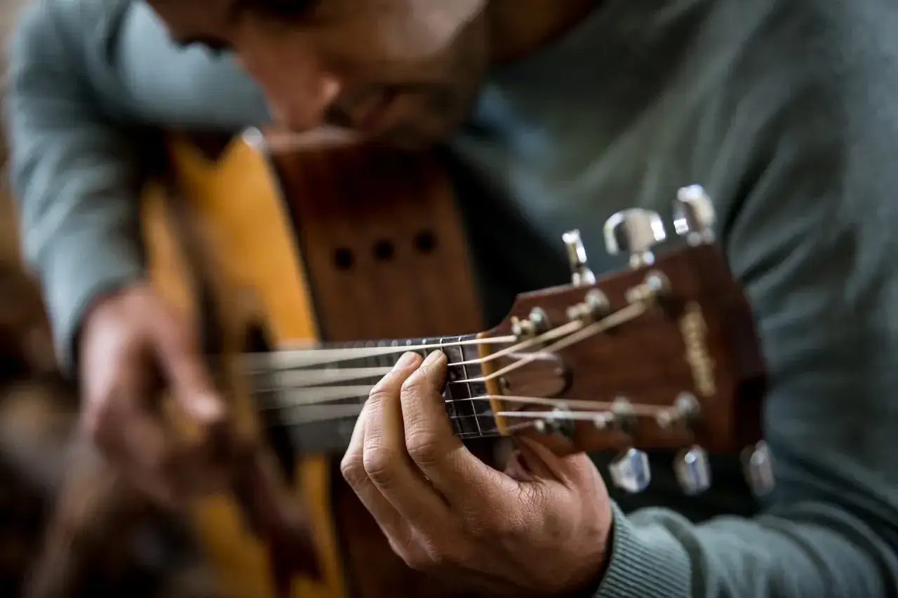 Mężczyzna gra na gitarze, jego palce tworzą akord. Słychać delikatne bicie harcerskie.