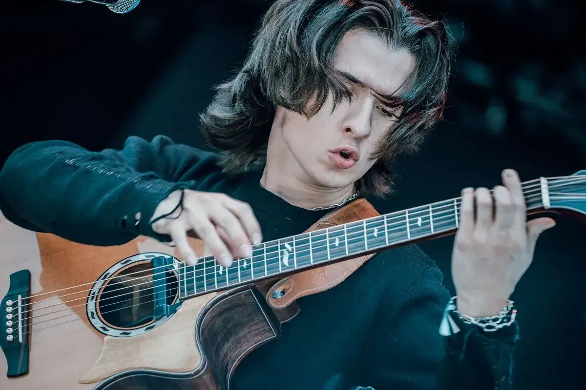 Marcin Patrzałek na koncercie, skupiony na grze na gitarze akustycznej.