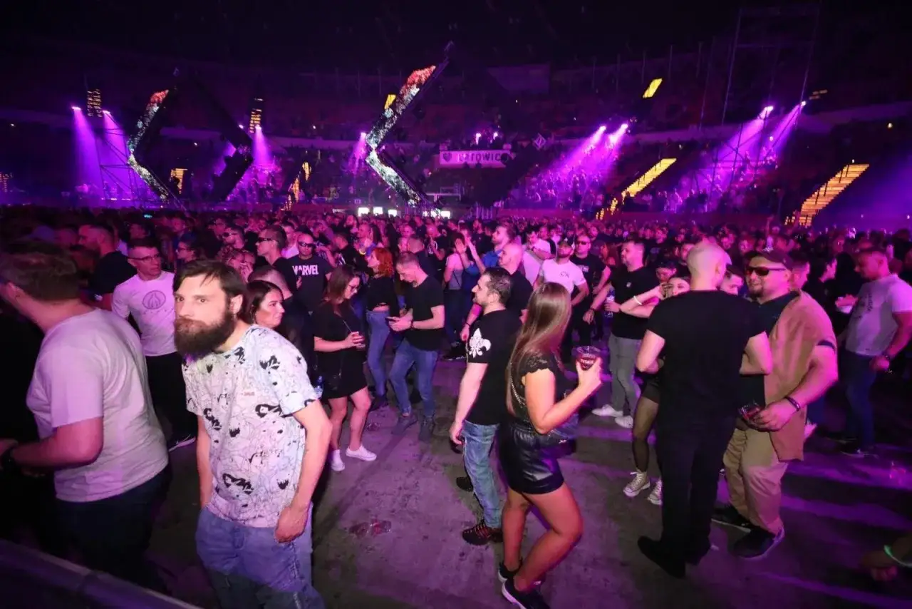 Tłum ludzi bawi się na mayday festiwal, otoczony fioletowymi światłami i imponującą scenografią.
