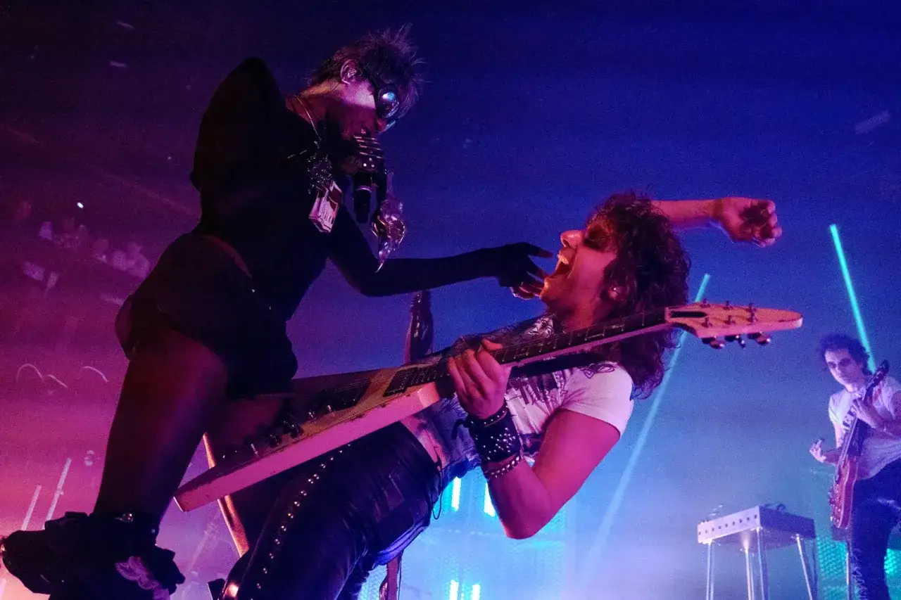 Energetyczny występ black midi na scenie. Wokalista z mikrofonem i gitarzysta z otwartymi ustami w szaleńczym geście.