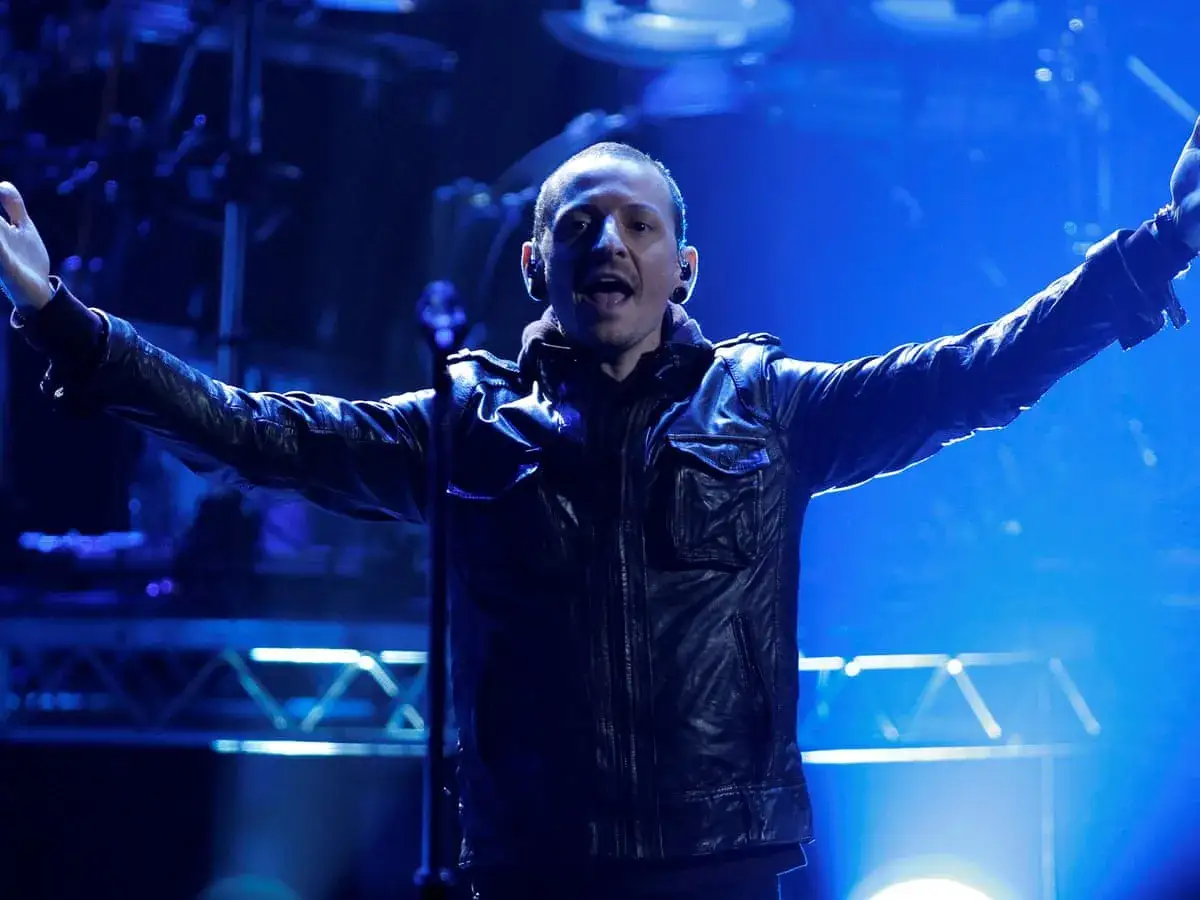 Chester Bennington z Linkin Park na scenie, w sk&oacute;rzanej kurtce, z rękami uniesionymi w geście radości.