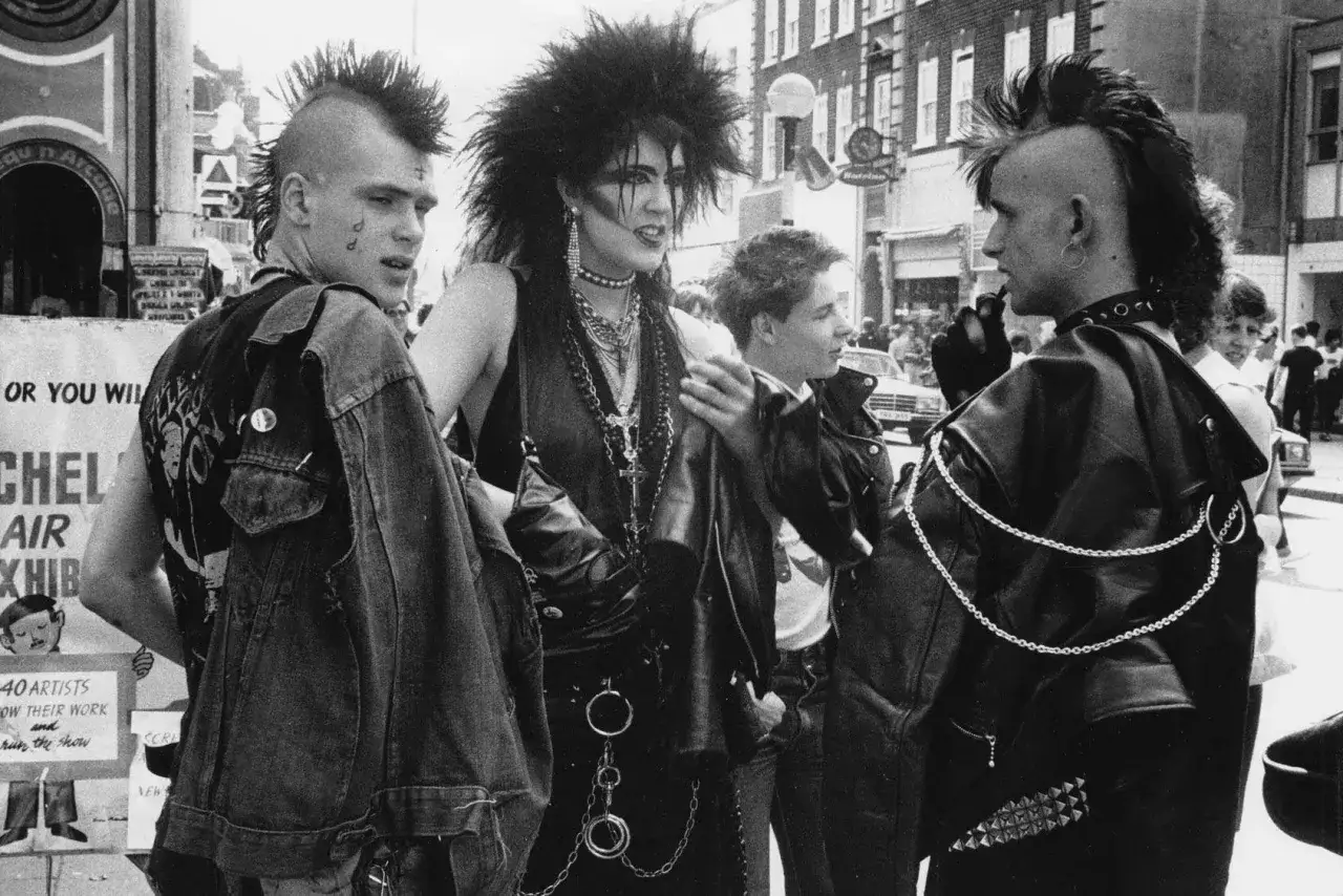 Młodzi ludzie z irokezami i w skórzanych kurtkach, uosabiający punk subkulturę, rozmawiają na ulicy.