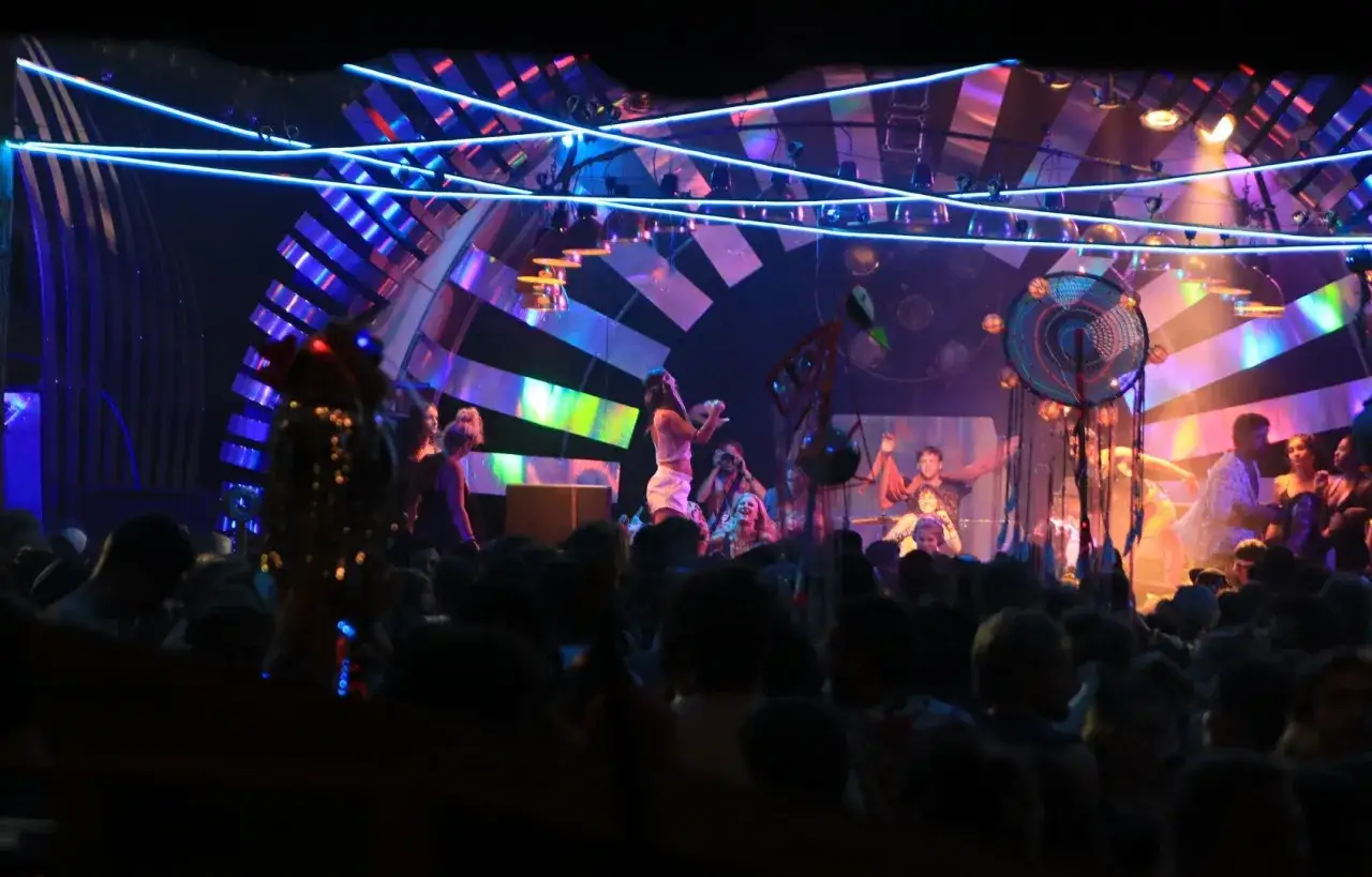 Tłum bawi się na Garbicz Festival pod neonowymi światłami. Na scenie artyści w kolorowych strojach.