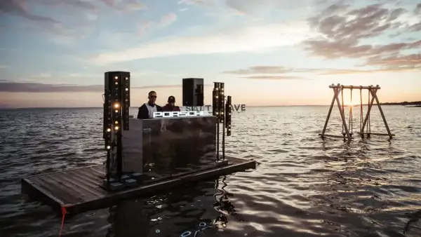 DJ na tratwie podczas zachodu słońca, z napisem "SALT WAVE" i huśtawką na wodzie.