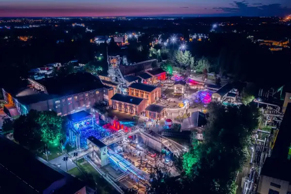 Nocny festiwal z kolorowymi światłami na terenie postindustrialnym. Ludzie bawią się na koncertach i stoiskach. To świetne miejsce na **carbon festival**!