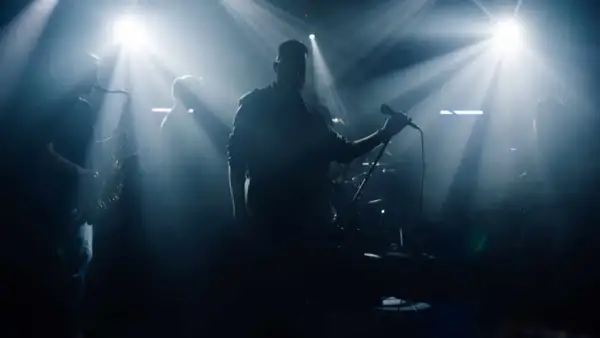 Zespół muzyczny na scenie, wokalista z mikrofonem, saksofonista, światła sceniczne.