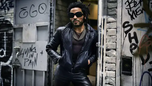 Lenny Kravitz w skórzanej kurtce i okularach, oparty o drzwi z graffiti, jakby właśnie wysiadł z łodzi.