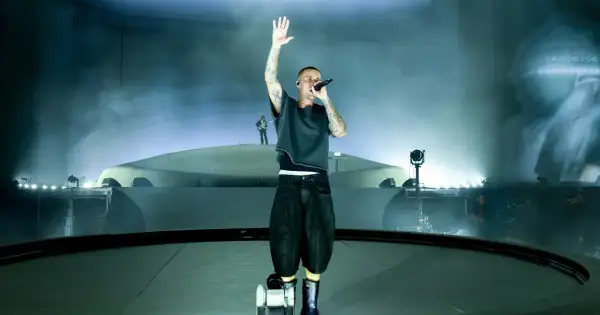 Justin Bieber śpiewa na scenie z podniesioną ręką, otoczony mgłą i światłami.