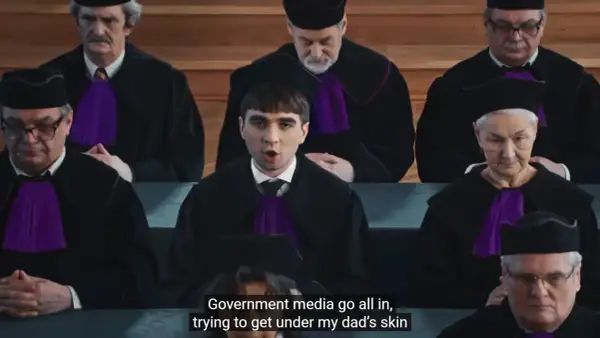 Młody mężczyzna w todze sądowej przemawia przed grupą sędziów w togach.