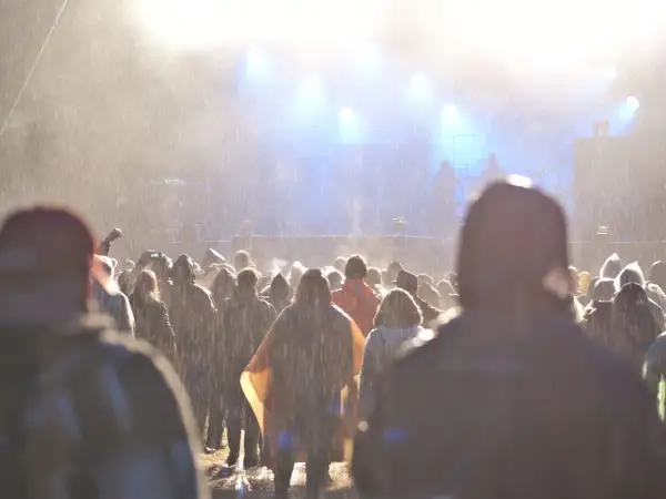 Tłum ludzi na festiwalu w deszczu, widok na scenę z oświetleniem.