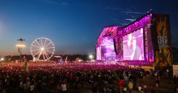 Koncert na Pol'and'Rock Festival z wielkim tłumem, sceną i diabelskim młynem w tle.