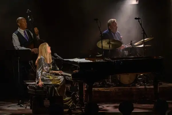 Diana Krall koncert: wokalistka i pianistka w błyszczącej sukni, kontrabasista i perkusista tworzą magiczną atmosferę jazzowego wieczoru.
