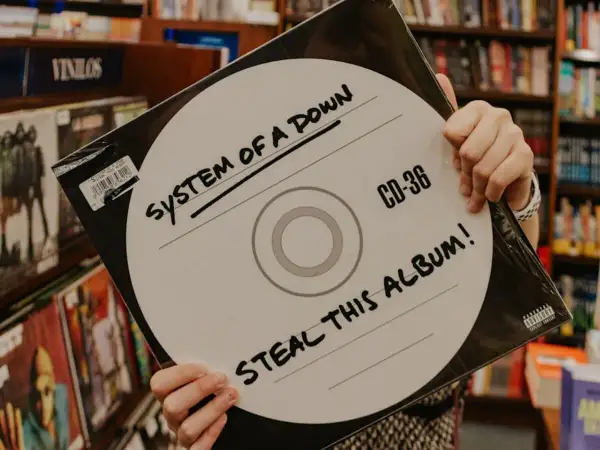 Ręce trzymają okładkę płyty System of a Down "Steal This Album!". Wybór między winylami a CD.