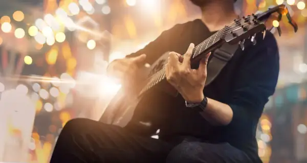 Mężczyzna grający na gitarze akustycznej na tle rozmytych świateł.