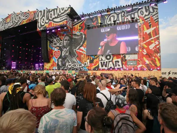 Tłum ludzi na koncercie Pol'and'Rock przed sceną z wielkim ekranem i grafikami.