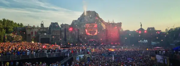 Tłum ludzi na jednym z największych festiwali muzycznych w Europie. Na scenie wulkanicznej wyświetlane jest imię Steve Angello, a nad głowami publiczności latają czerwone konfetti.