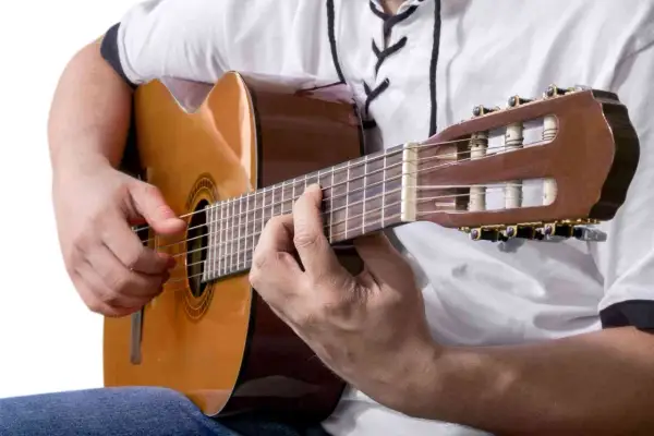 Dłonie grają na gitarze klasycznej, tworząc akordy. To może być najłatwiejsza piosenka na gitarze, którą właśnie ćwiczysz.