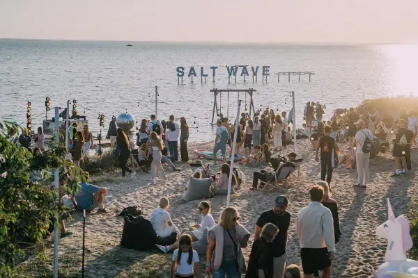 Ludzie na plaży podczas festiwalu Salt Wave, z napisem "SALT WAVE" nad wodą.