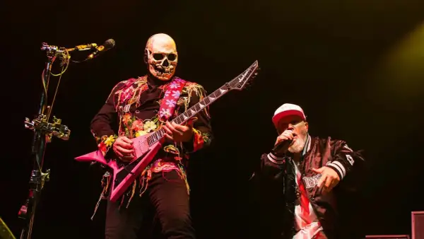 Muzyk w masce czaszki gra na różowej gitarze, wokalista w czapce śpiewa na scenie podczas impact festival.