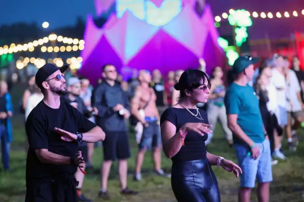Ludzie tańczący na festiwalu Audioriver w Łodzi, z kolorową scenografią w tle.