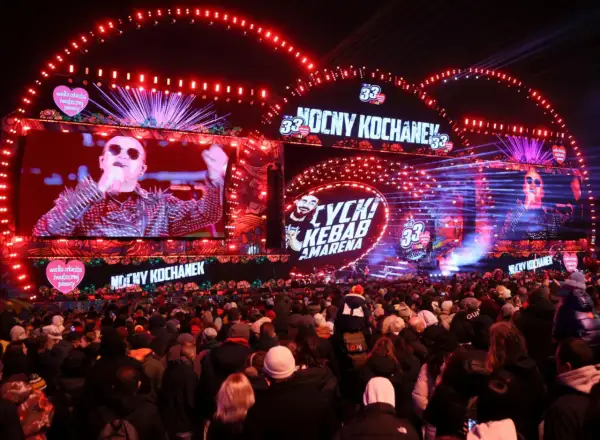 Koncert WOŚP 2026: tłumy ludzi pod sceną, na ekranach artyści, czerwone światła i serca WOŚP.