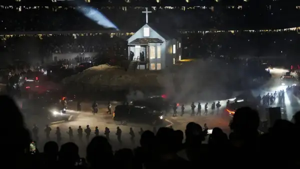 Scena z koncertu Donda 2: biały kościół z krzyżem na dachu, otoczony dymem, ludźmi i samochodami, w blasku reflektorów.