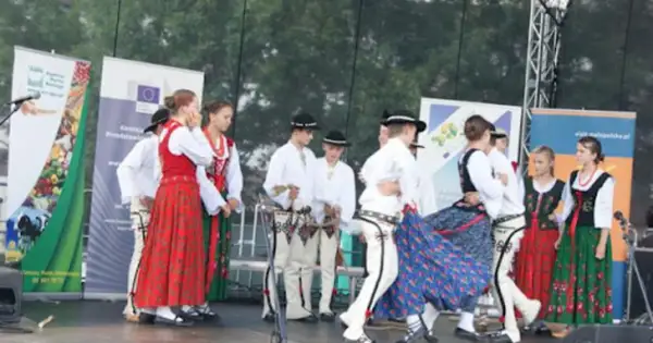 Grupa ludzi w tradycyjnych strojach ludowych tańczy na scenie.