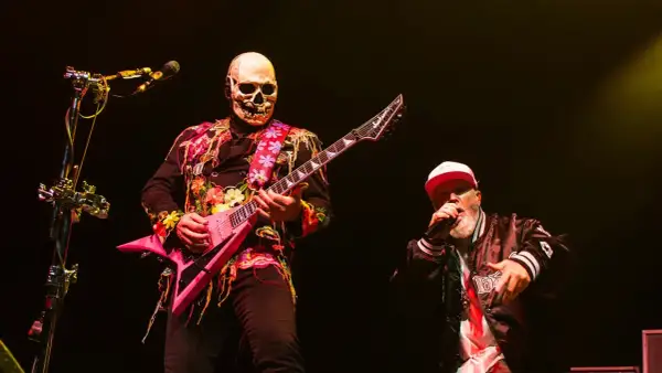 Muzyk w masce czaszki gra na różowej gitarze, a wokalista w czapce śpiewa na koncercie Limp Bizkit.