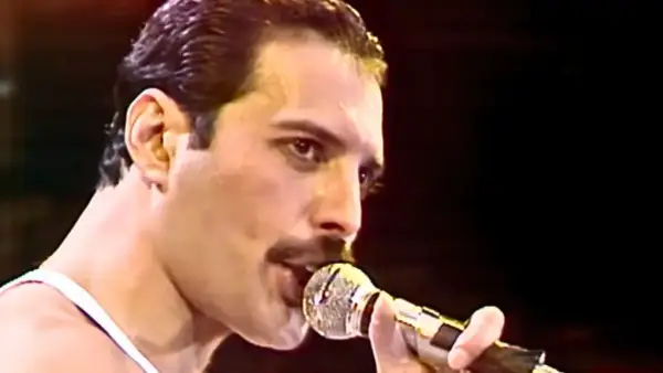 Freddie Mercury śpiewający do mikrofonu na scenie.
