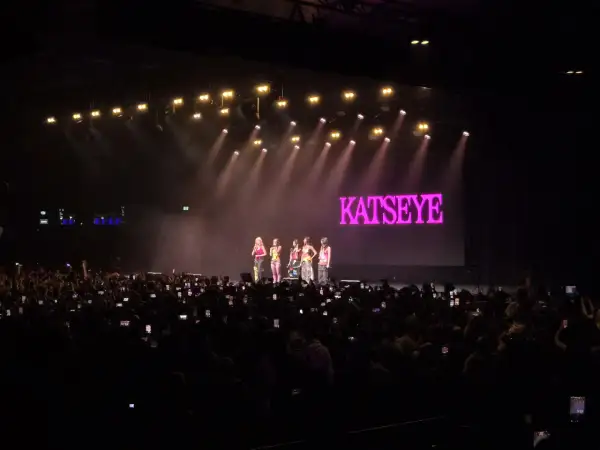 Koncert dziewczęcej grupy Kátseye, publiczność z telefonami, różowe światła i logo zespołu na ekranie.