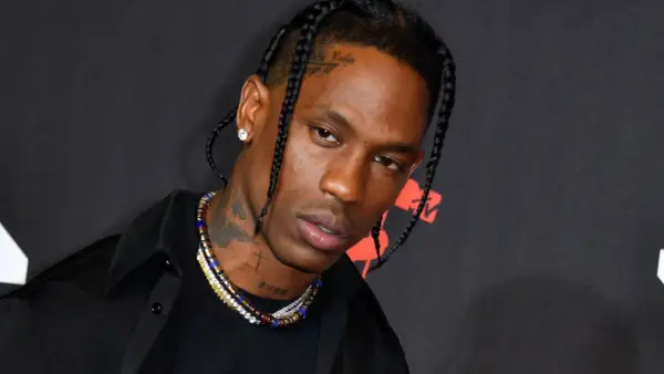 Travis Scott w czarnej koszuli i z warkoczami, z naszyjnikami i tatuażami na szyi.